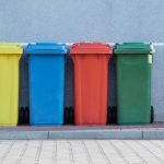 Recycling Bins - four assorted-color trash bins beside gray wall