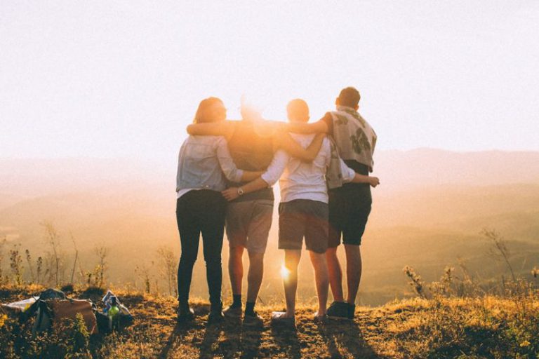 Happy Volunteers - four person hands wrap around shoulders while looking at sunset