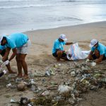 Beach Cleanup - man in teal t-shirt and white shorts sitting on brown sand near sea during daytime