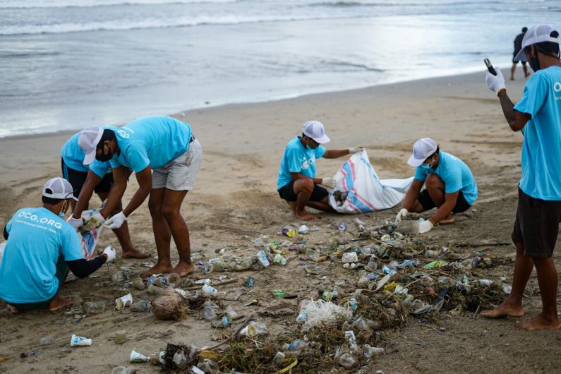 Beach Cleanup - man in teal t-shirt and white shorts sitting on brown sand near sea during daytime