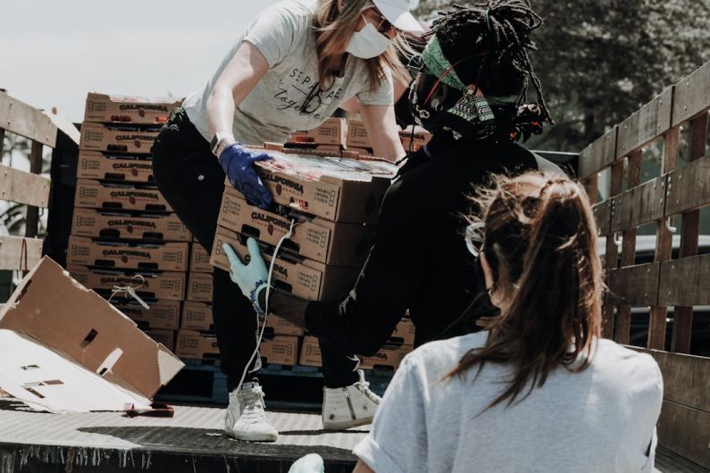 Charity - woman in white t-shirt and blue denim jeans sitting on brown cardboard box